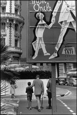 CANNES, France—Jacques Tati and Alain Bercourt walk toward the Hotel Carlton, which bears a poster for Tati’s Mon Oncle, playing at the Cannes Film Festival, 1958. © Henri Cartier-Bresson / Magnum Photos